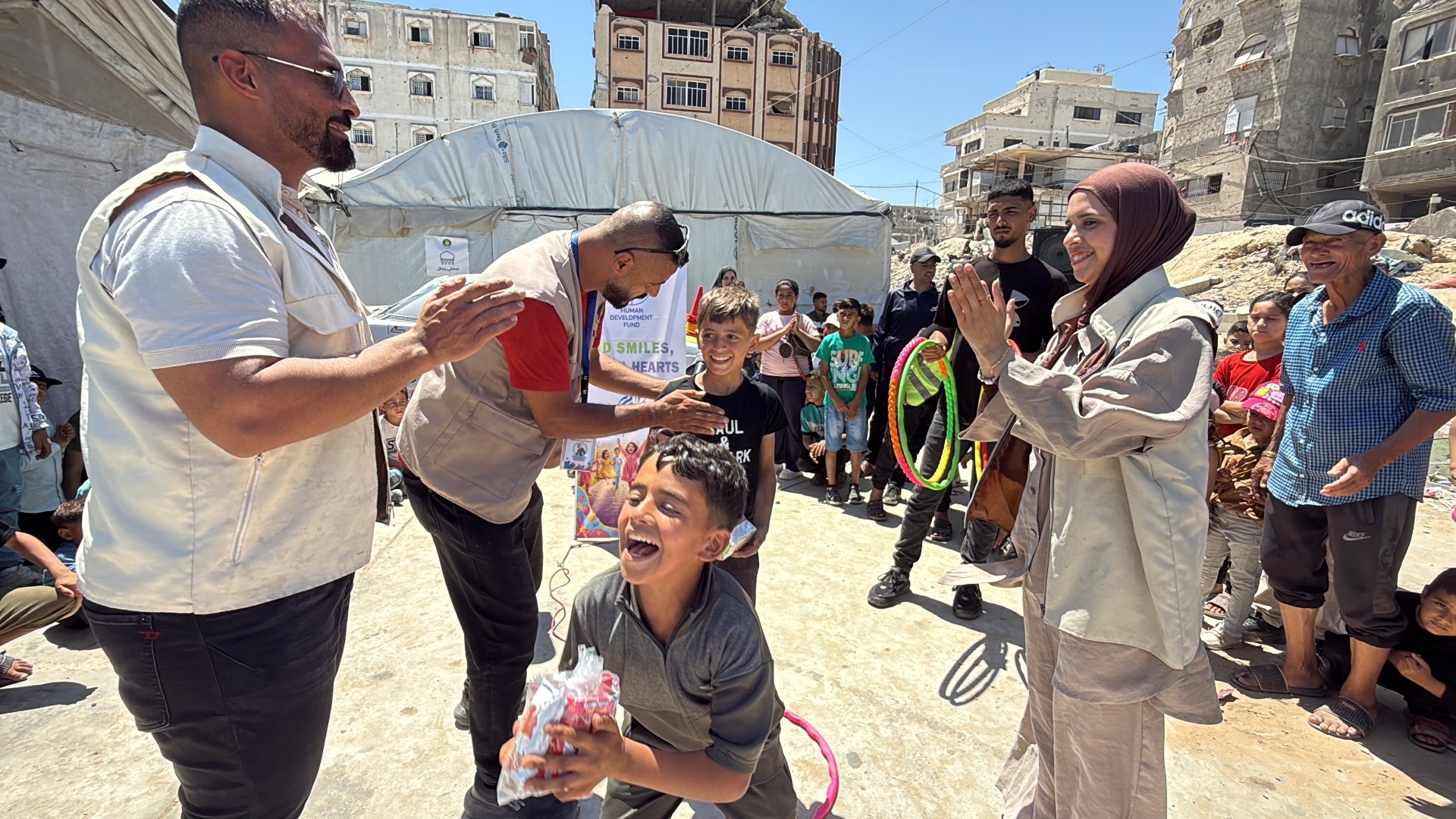 A boy laughing with joy while HDF team members and a friend celebrate around him at the Eid celebration in Gaza.