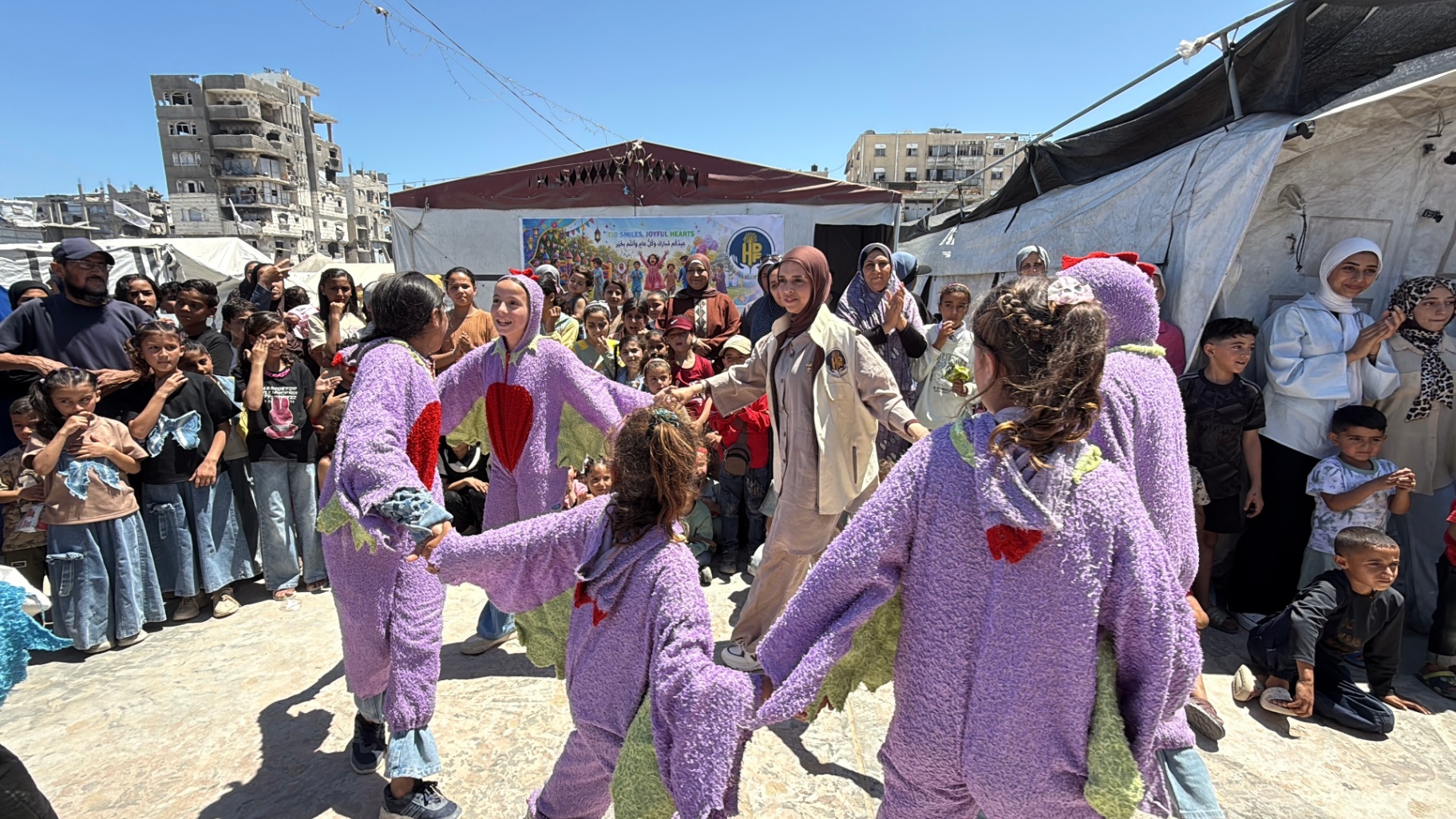 Children in purple costumes dancing in a circle at HDF's Eid Smiles, Joyful Hearts celebration in Gaza.