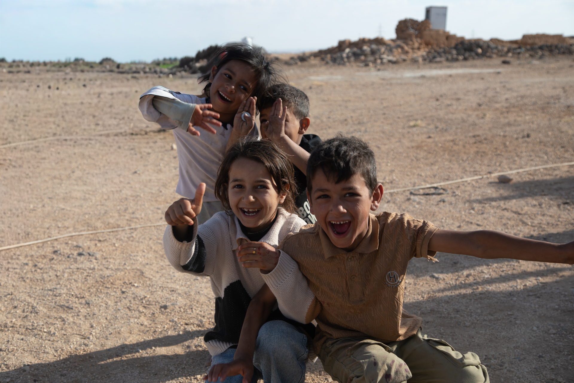 Four children from beneficiary families smiling and waving outdoors during HDF's Qurbani meat distribution in Jordan.