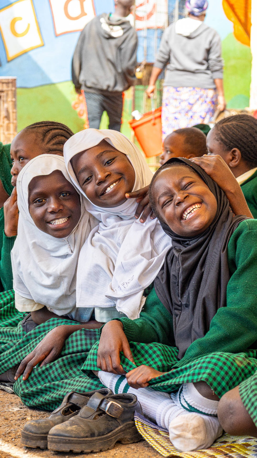 Three young girls in hijabs hugging and laughing together at HDF's Eid celebration in Kenya.