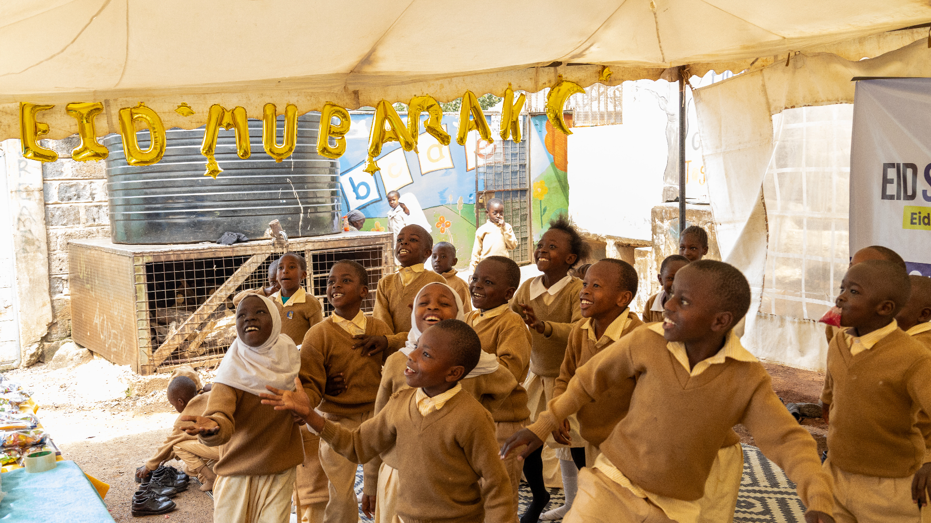 Children laughing and cheering beneath a gold Eid Mubarak balloon banner at HDF's Eid celebration in Kenya.