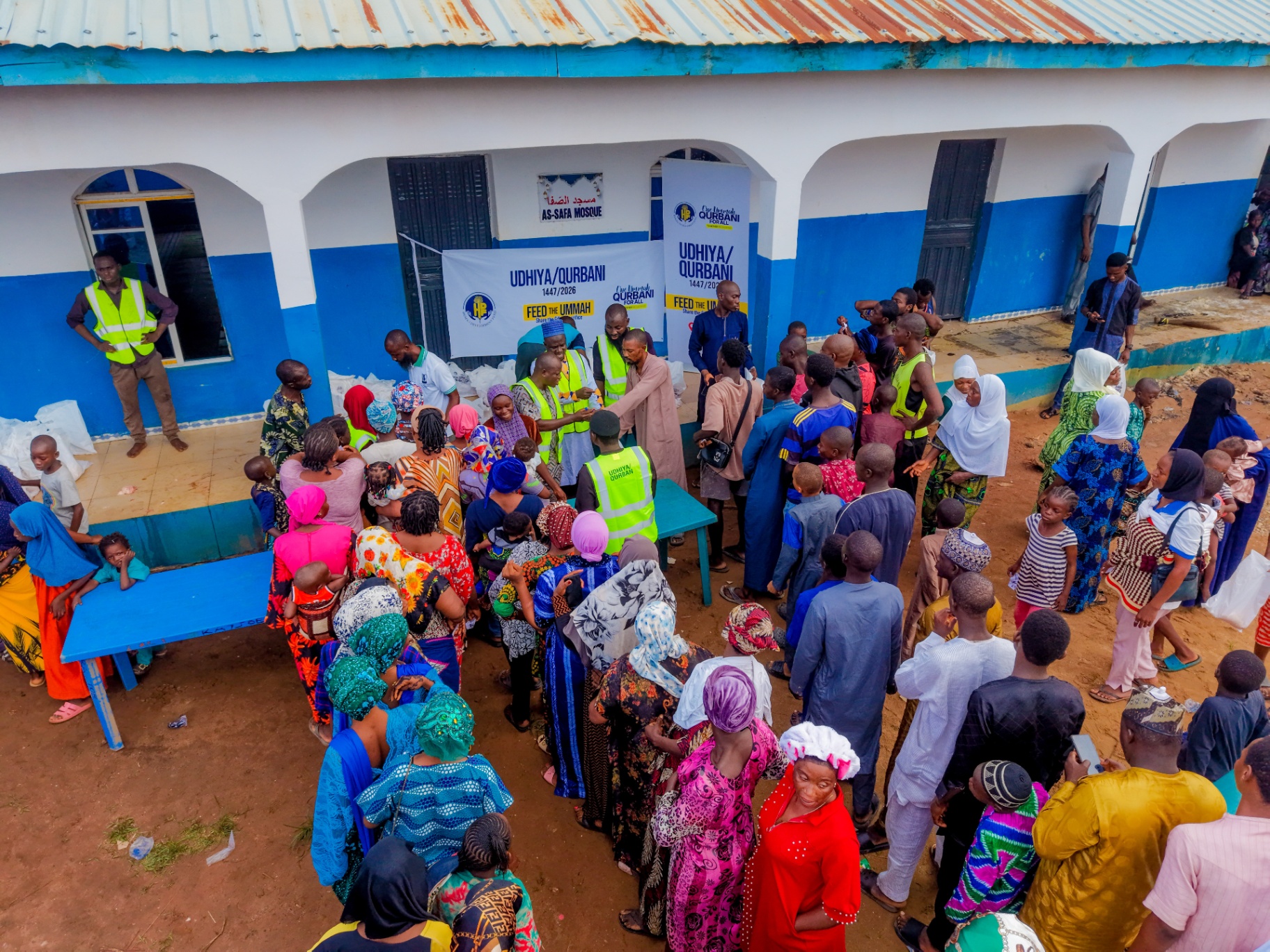 Aerial view of families and children lined up beside the HDF Udhiya / Qurbani — Feed the Ummah distribution outside the blue and white As-Safa Mosque in Nigeria.