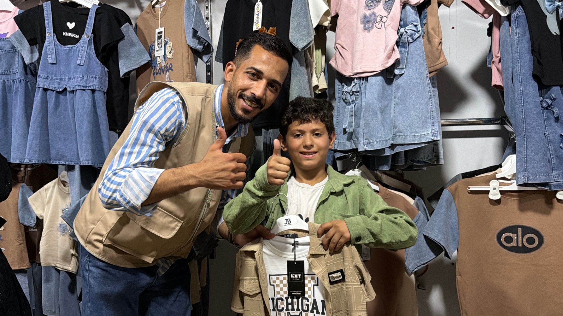 A boy smiling with an HDF volunteer while holding his new Eid outfit in Gaza.