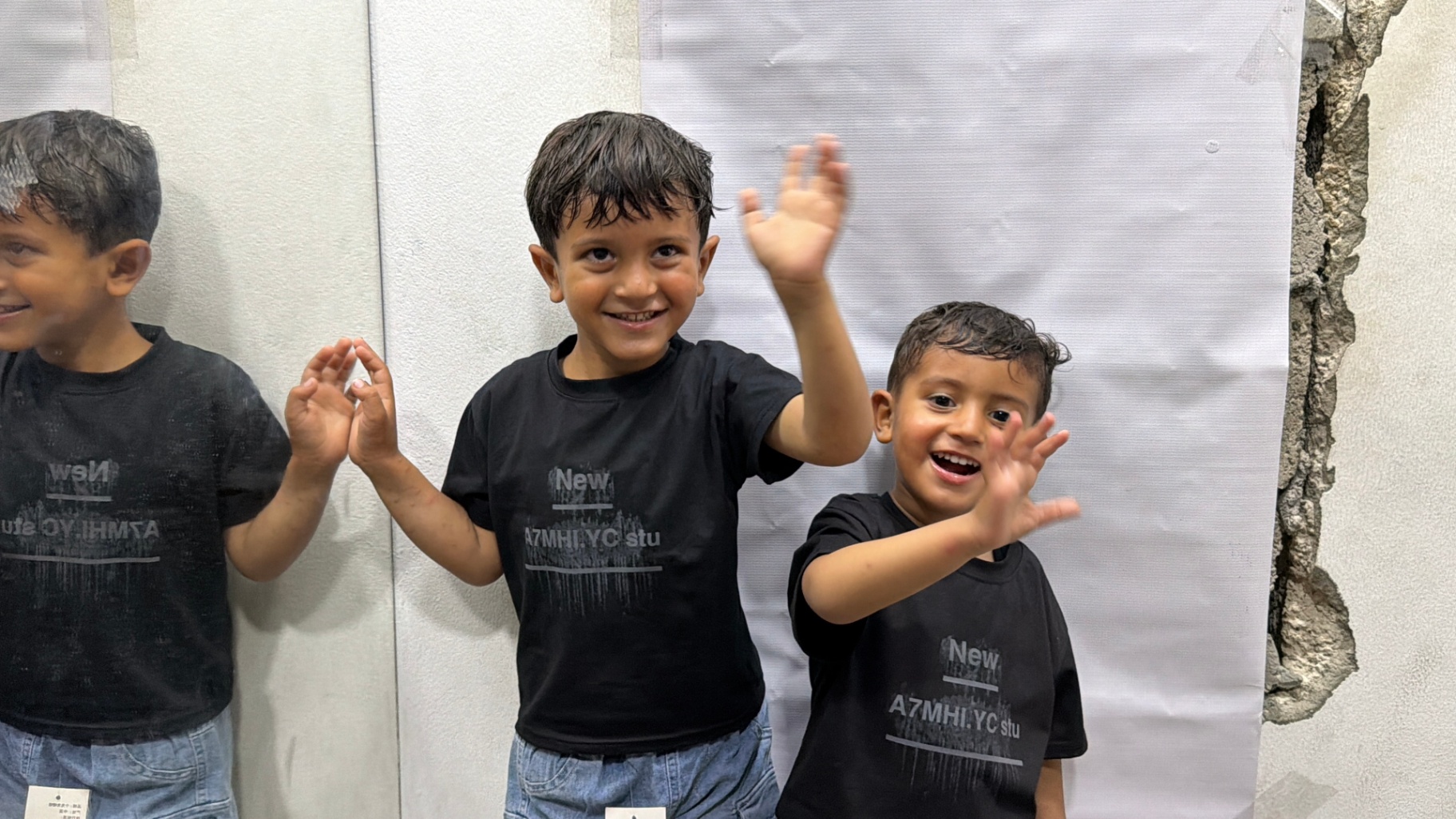 Two boys smiling and waving after receiving new Eid clothing through HDF's Gaza program.