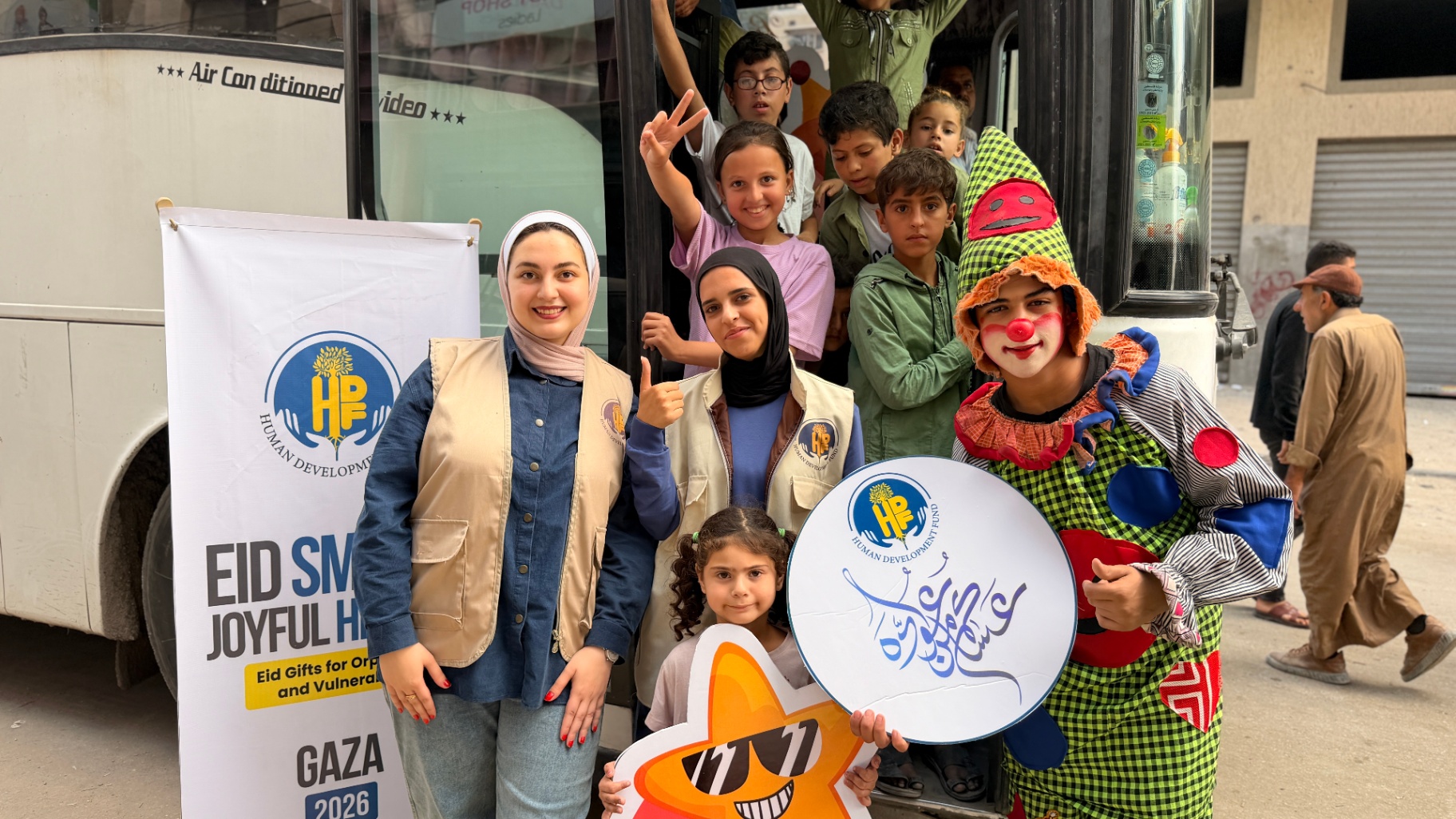 HDF volunteers, children, and a performer gathered by the bus at the start of the Gaza Eid outing.