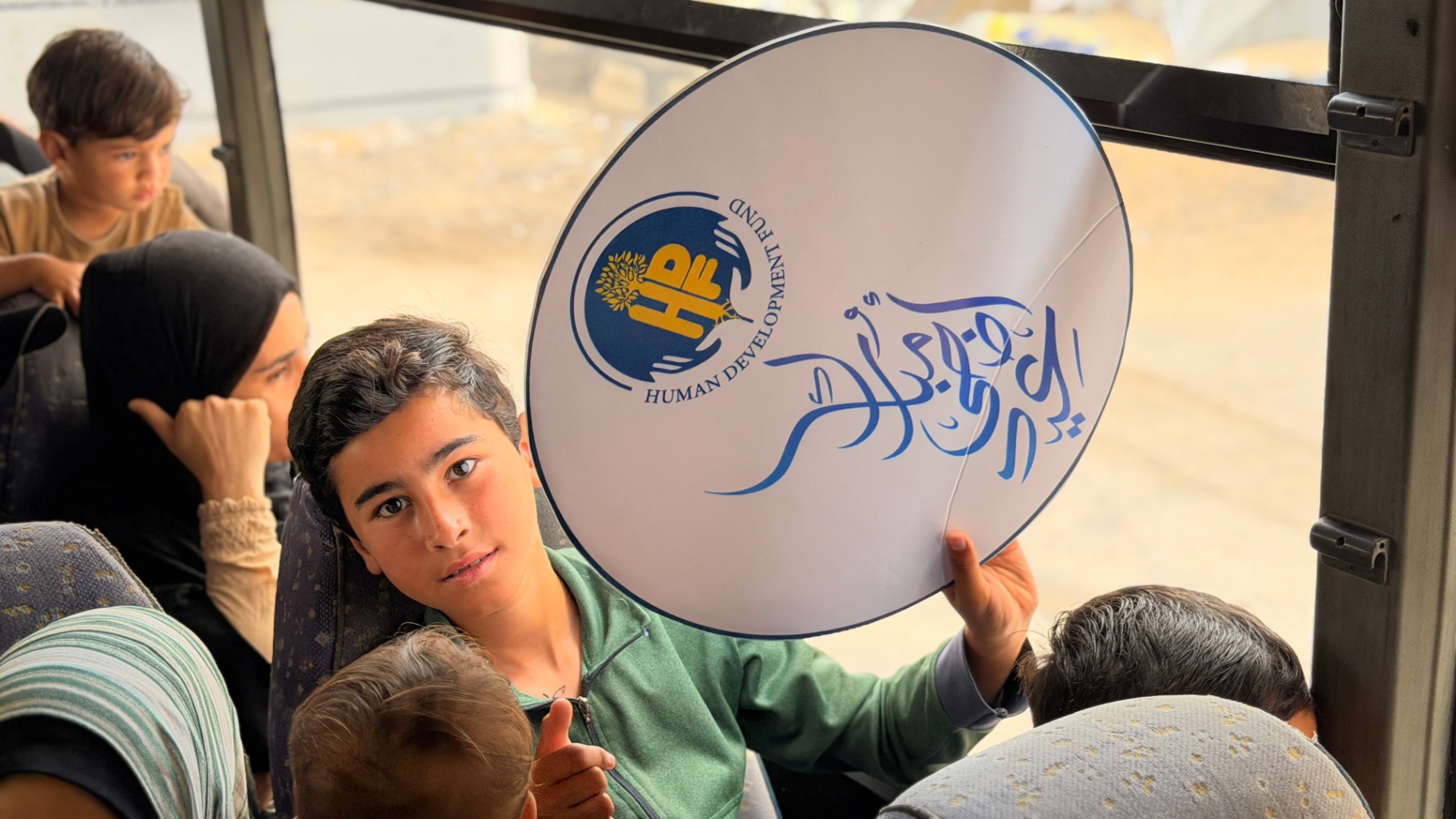 A child on the bus holding an HDF Eid sign during the pre-Eid outing in Gaza.
