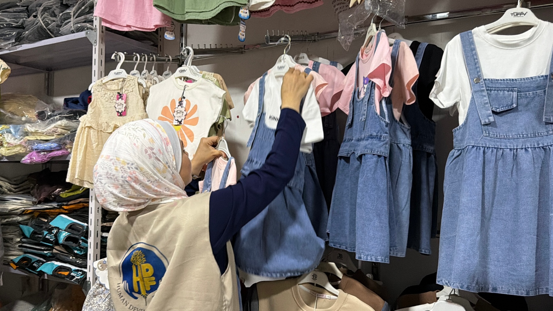 An HDF volunteer choosing clothing from a rack during the pre-Eid shopping program in Gaza.