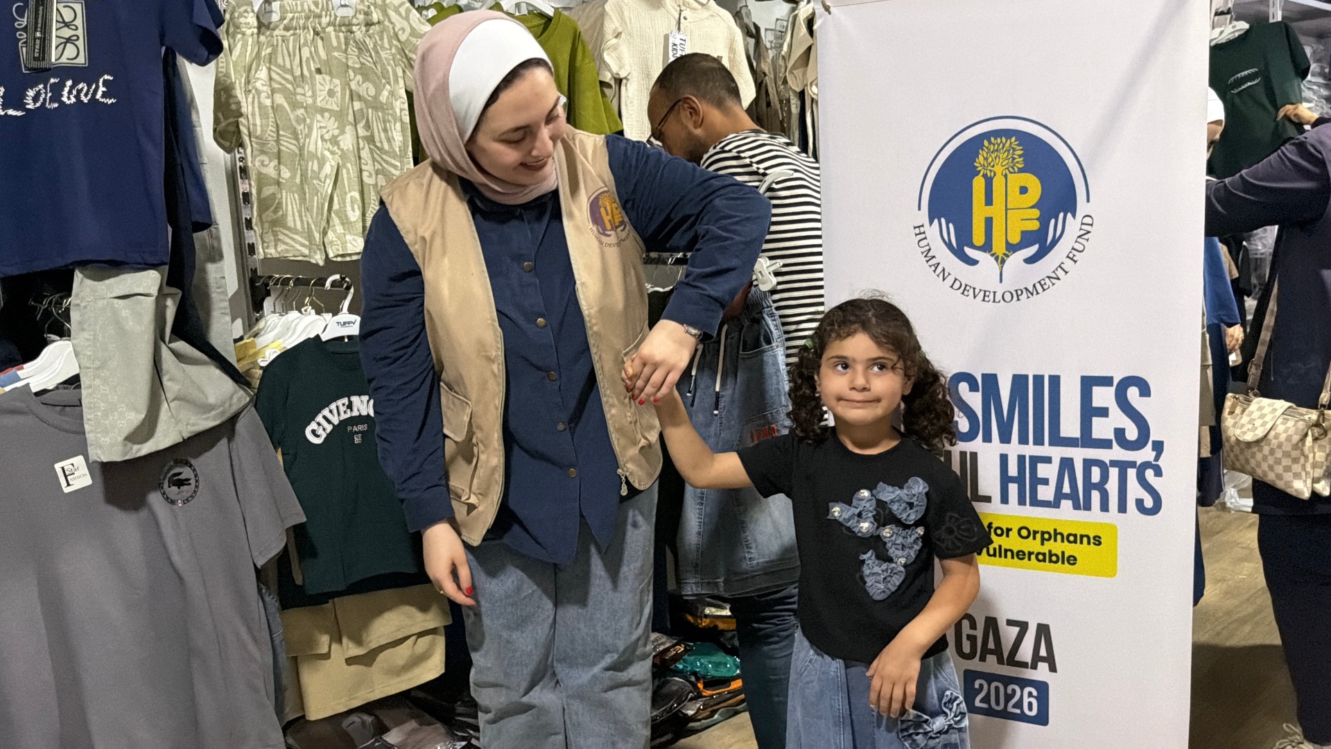 A young girl standing with an HDF volunteer during the pre-Eid shopping program in Gaza.