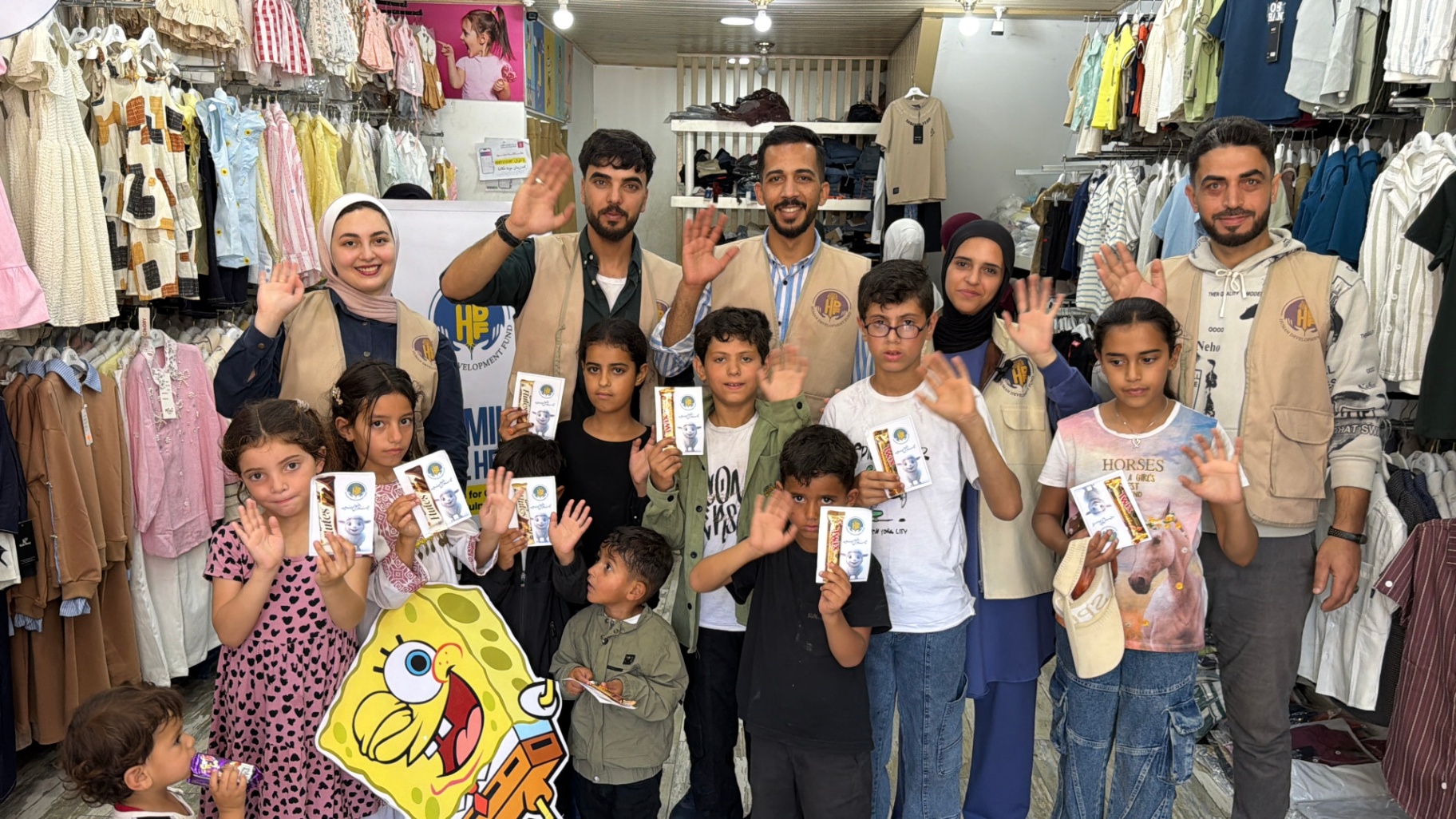 A group of children and HDF volunteers waving together inside the clothing store after the Gaza outing.