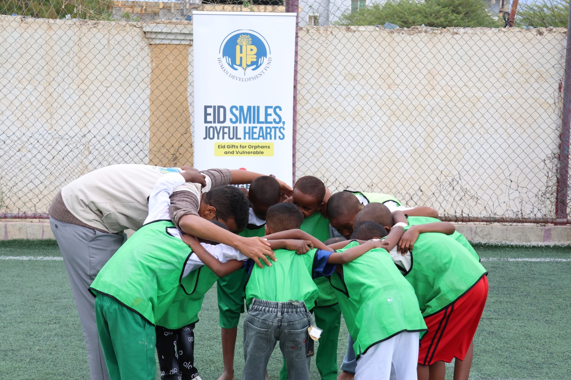 Boys in green jerseys huddled together in front of the Eid Smiles, Joyful Hearts banner in Hargeisa, Somalia.