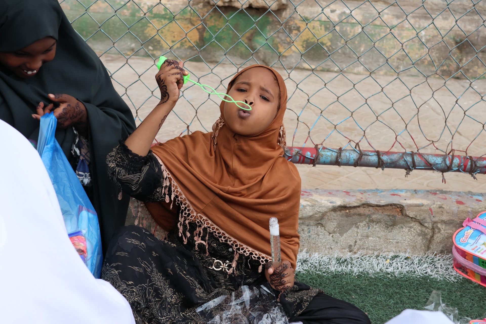 A young girl in an orange hijab blowing bubbles with henna-decorated hands at HDF's Eid celebration in Somalia.