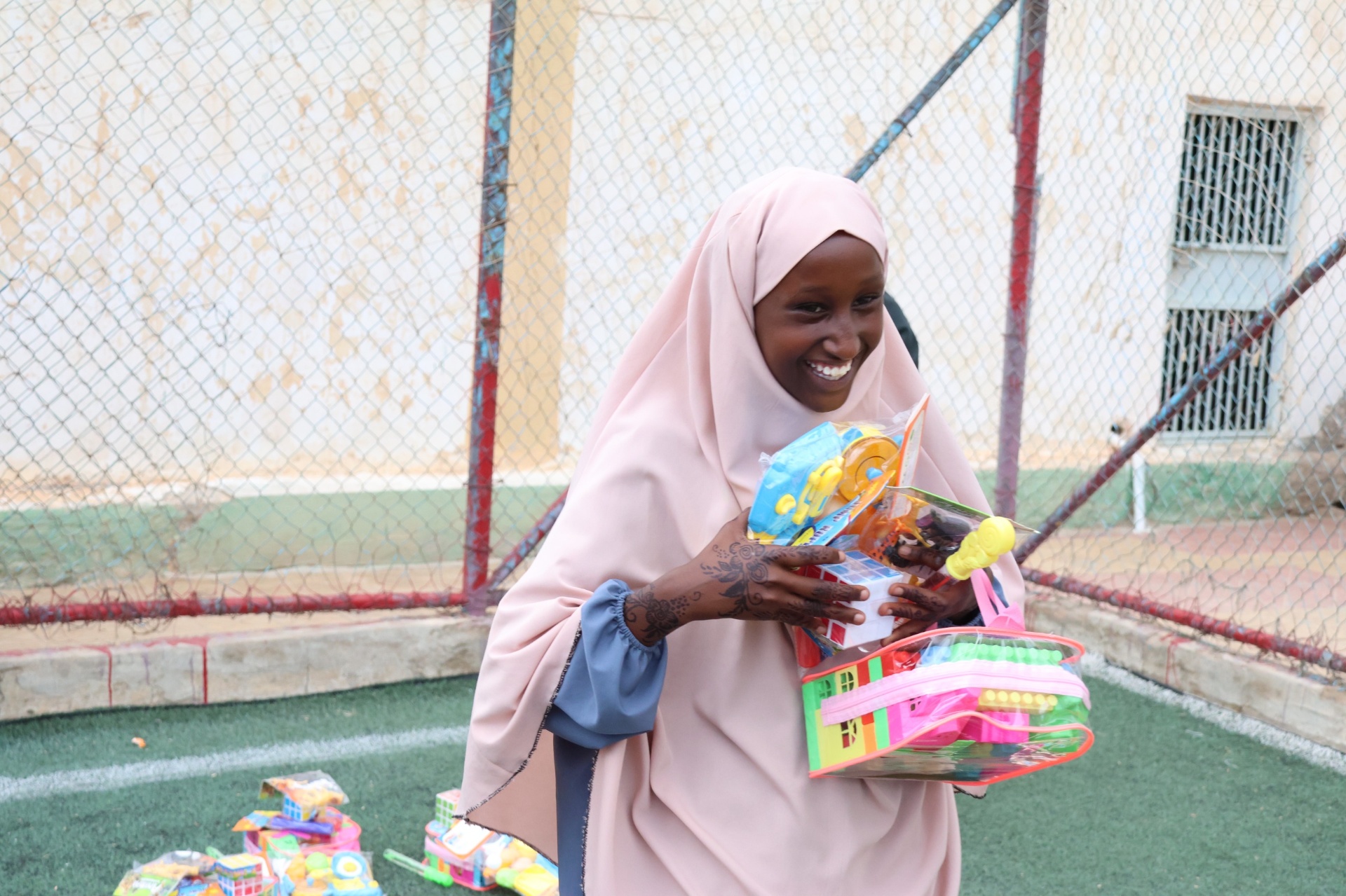 A girl in a pink hijab smiling brightly while holding a basket of Eid toys in Hargeisa, Somalia.